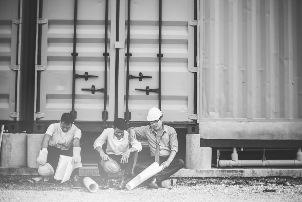 three construction workers sitting beside a building and resting after work