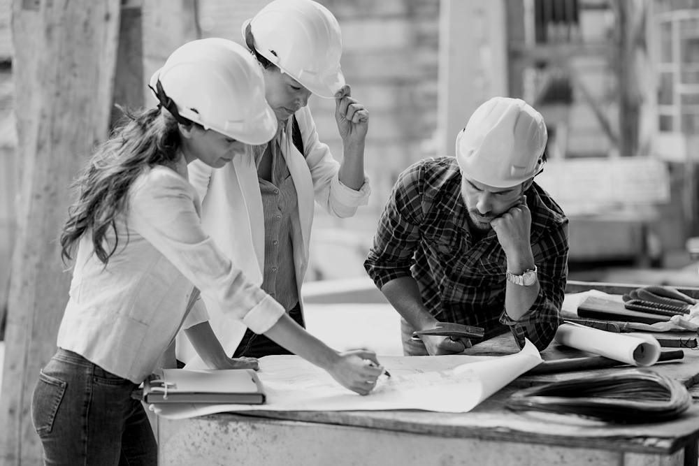 two female construction workers in hard hats reviewing design plans with male construction worker