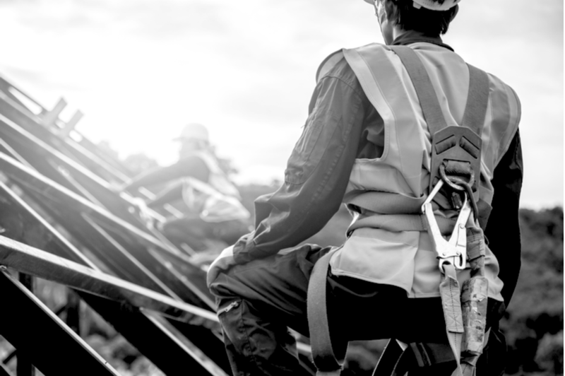 [safety body construction] Working at height equipment. Fall arrestor device for worker with hooks for safety body harness on selective focus. Worker as in construction background.