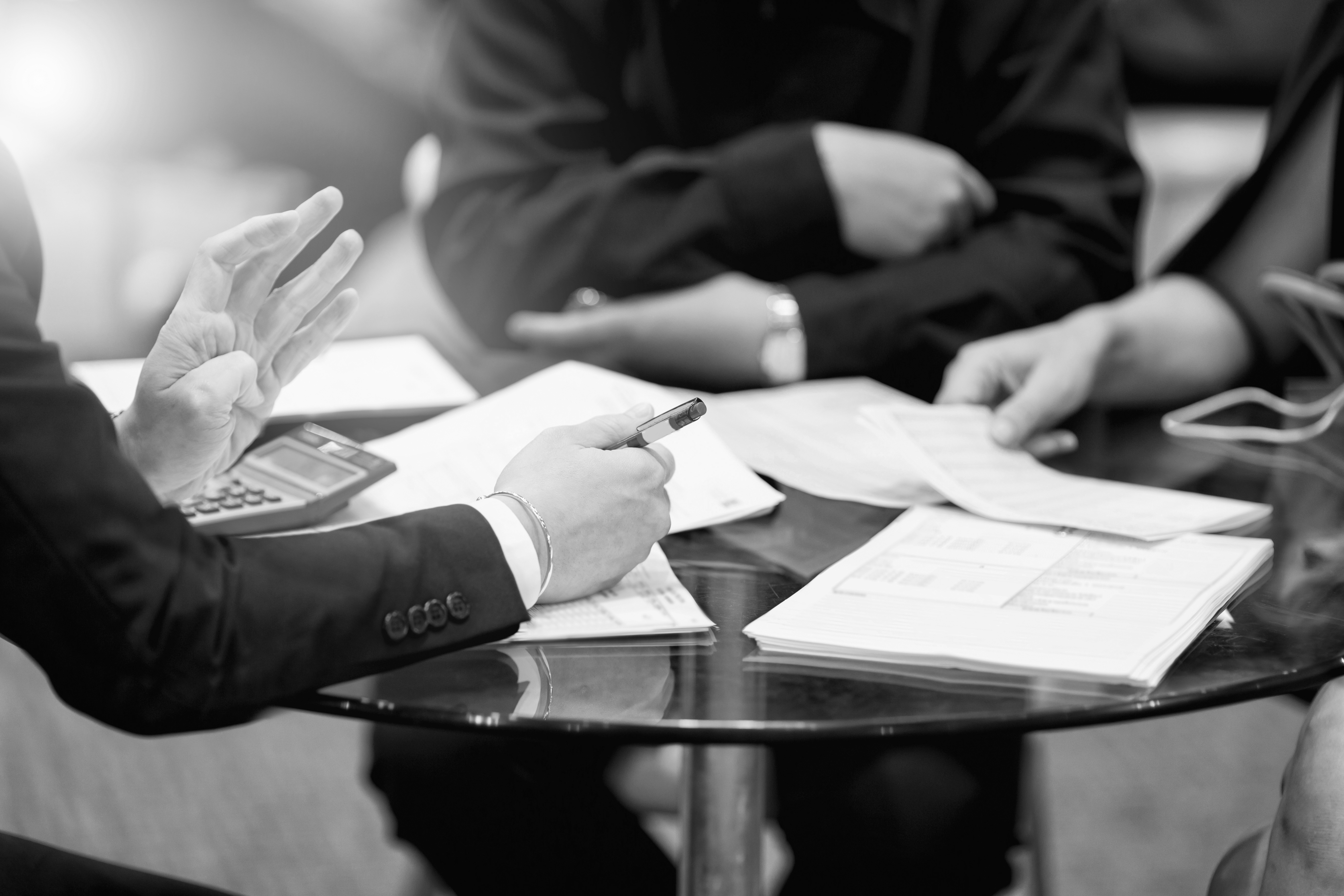 Three people sitting around a table, meeting and discussing with papers in front of them.